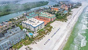 Luftaufnahme einer Küstenlandschaft mit Strand, Fluss und mehreren Gebäuden, darunter ein Hotel mit mehreren Etagen und Balkonen.