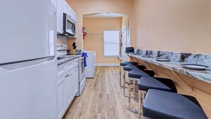 Une cuisine compacte avec des meubles blancs, un four à micro-ondes, un petit four et un comptoir agrémenté de tabourets de bar.