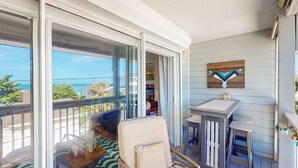 A balcony with a view of the ocean, a chair, a small table, and a wall-mounted artwork. - Gulf view and stunning sunsets family friendly steps from beaches WD and WIFI (Indian Rocks Beach)