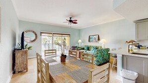A spacious living area with a wooden dining table, a sofa, and a ceiling fan. - Water view condo with pool hot tub pier private balcony AC and washer dryer (Treasure Island)