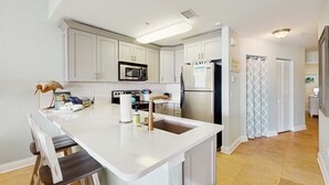 A modern kitchen with white cabinets, a stainless steel refrigerator, a microwave, and a sink. - Water view condo with pool hot tub pier private balcony AC and washer dryer (Treasure Island)