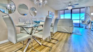 Un espace de salle à manger moderne avec une table en verre, des chaises chromées et un lustre.