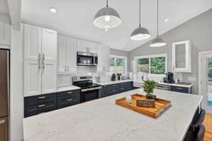A modern kitchen with white cabinets, a marble island, and pendant lighting. - Luxe Blue Haven 3BR + Sleeps 8 + Huge Fenced Yard (Durham)