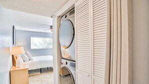 A laundry room with a washing machine, a dryer, and a bed with a nightstand. - Quiet Waves 20 Condo with Pool Steps to Dining Shopping and St Pete Beach (St. Pete Beach)
