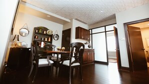 A dining area with a wooden table and chairs, a kitchen with dark wooden cabinets, and a white ceiling with a textured pattern.