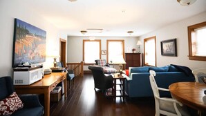 A spacious living room with a wooden dining table, blue sofas, and a large painting on the wall.