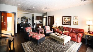 A living room with a red sofa, black armchairs, and a patterned rug. There is a dining area with a table and chairs, and a kitchen with cabinets and a microwave.