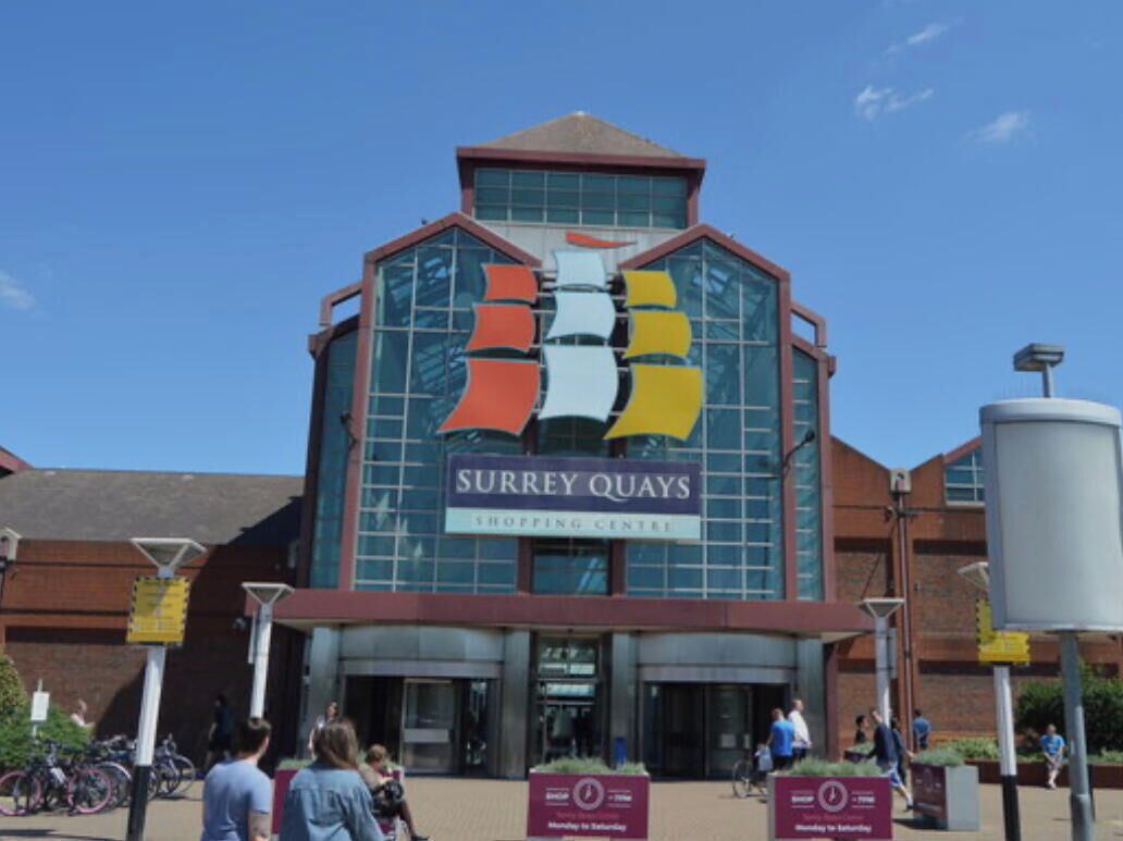Esterno del centro commerciale Surrey Quays, con un grande cartello e facciata in vetro.