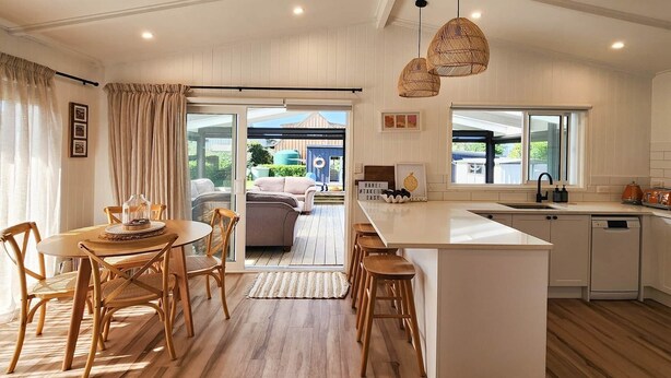 A modern kitchen with a central island, wooden flooring, and a dining area with a round table and chairs. - Seashell Cottage - cosy, newly renovated, central, close to shops and beach (Hahei)