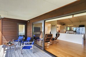 A modern outdoor seating area with wooden flooring and glass doors leading to a kitchen.