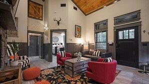 A spacious living room with a fireplace, red armchairs, a coffee table, and a large window. - Romantic Cabin | Hot Tub · Gas Grill · Fireplace (Broken Bow)