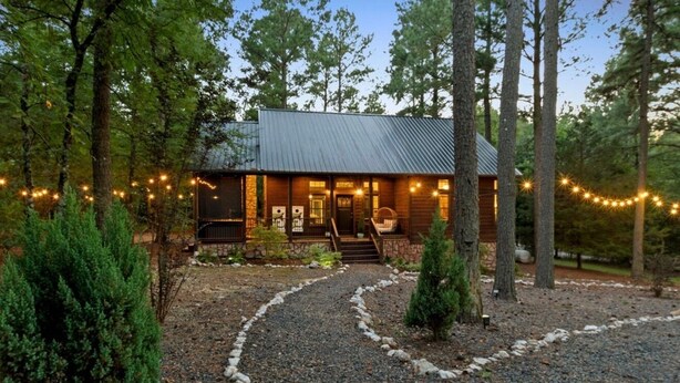 A rustic cabin with a metal roof, surrounded by trees and a gravel path leading to the entrance. - Romantic Cabin | Hot Tub · Gas Grill · Fireplace (Broken Bow)