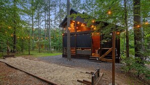 A cabin with a wooden deck, surrounded by trees and gravel. - Romantic Cabin | Hot Tub · Gas Grill · Fireplace (Broken Bow)