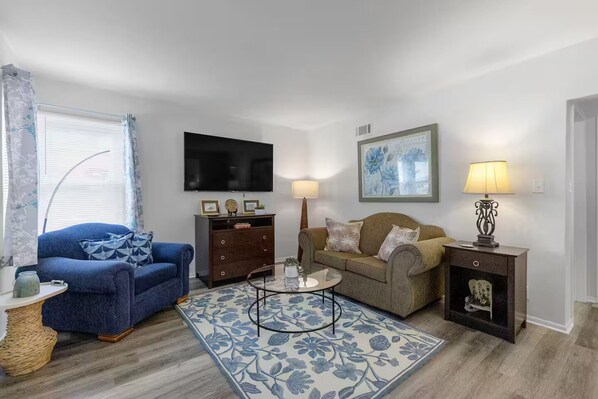 A living room with a blue sofa, a brown sofa, a coffee table, a TV, a lamp, and a framed picture on the wall. - Modern Garden 1BR | Laundry + Pets OK | Quiet (Saint Joseph)