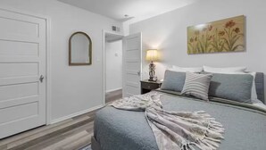 A bedroom with a bed, bedside table, lamp, and a painting on the wall.