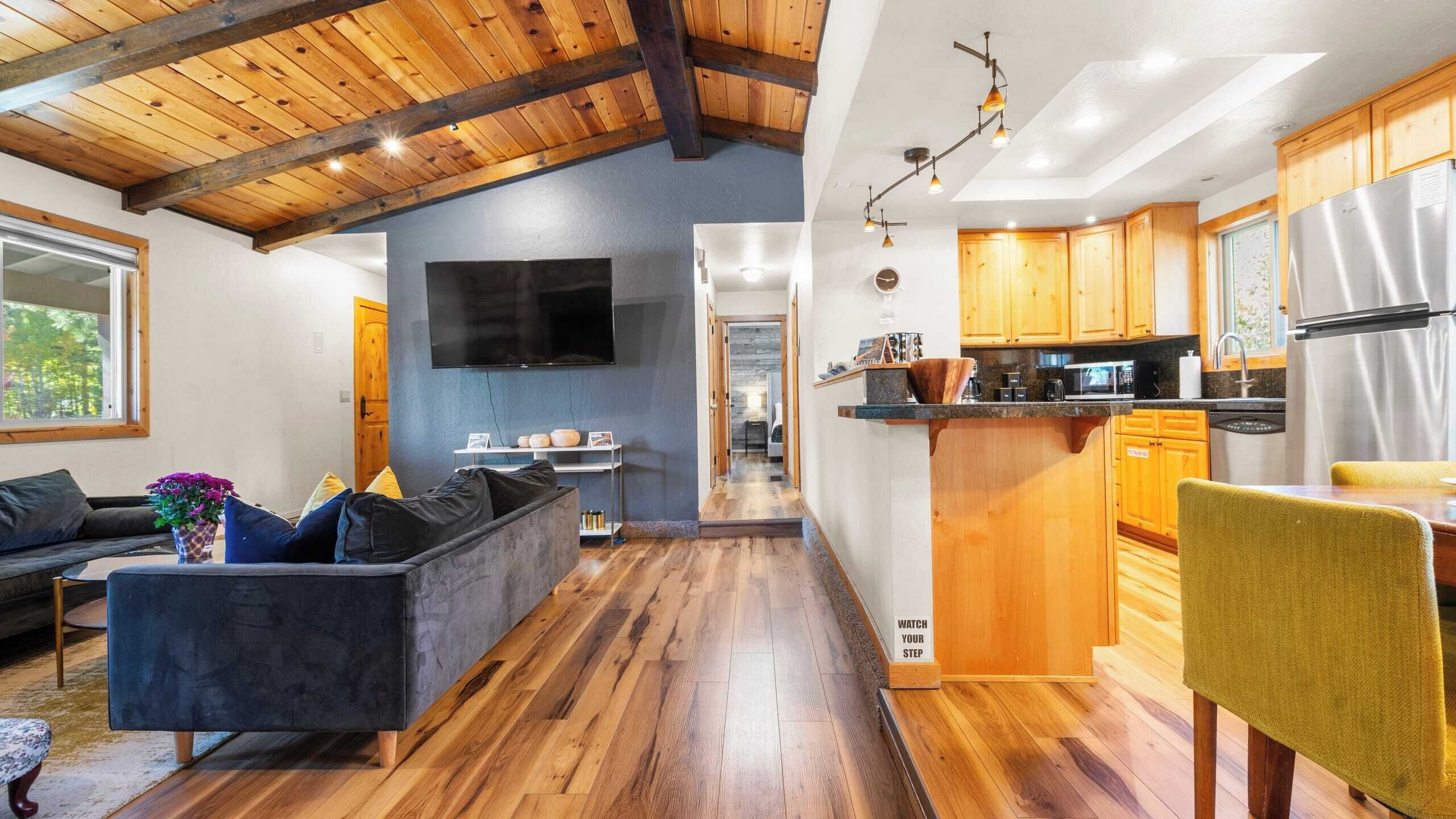 Un interior moderno con techo de madera, una sala de estar con sofá y televisor, y una cocina con armarios y electrodomésticos de madera.