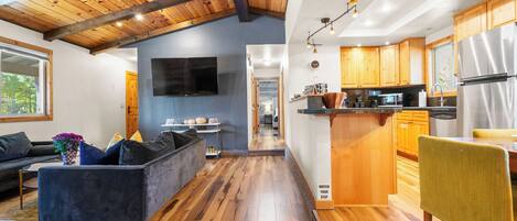 Un interior moderno con techo de madera, sala de estar con sofá y televisor, cocina con gabinetes de madera y comedor con mesa y sillas.