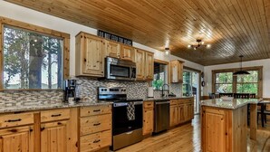 Cucina con mobili in legno, forno a microonde, piano cottura e un'ampia finestra con vista sugli alberi.
