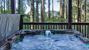Una vasca idromassaggio con cascata, circondata da un pontile in legno e alberi alti.