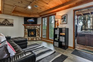 A cozy living room with a stone fireplace, a black leather sofa, and a bookshelf.