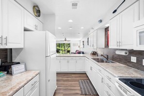 A modern kitchen with white cabinetry, a marble countertop, and a view of the outdoors. - Stay & Play Branson Basecamp (Branson)