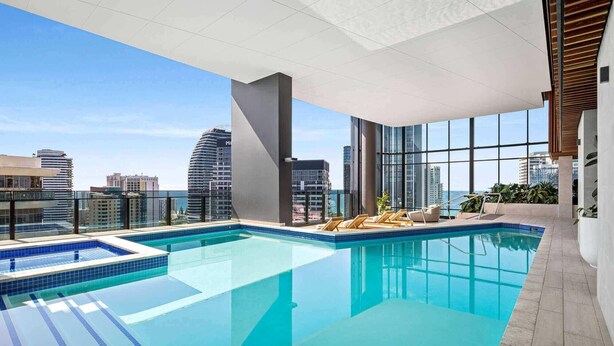 A rooftop infinity pool with clear blue water, surrounded by large windows offering city views. - Comfy 1 Bedroom Unit with River/City View - Q Stay (Broadbeach)