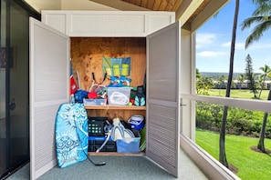 A room with a wooden wall, a window with a view of palm trees, and a shelf with sports equipment. - Kksr#6301 Ocean/golf Course Views, Top Floor (Kailua-Kona)