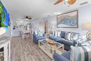 Un salon moderne avec un canapé bleu, une table basse en verre et un coin repas comprenant une table et des chaises blanches.