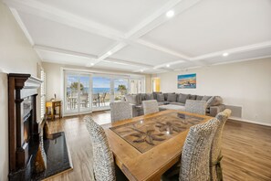 Een ruime woonkamer met een open haard, een grote houten salontafel en uitzicht op de oceaan door grote schuifdeuren.