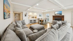 A spacious living room with a grey sectional sofa, a fireplace, and a dining area with a kitchen in the background.