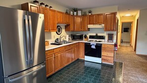 Una cocina moderna con armarios de madera, electrodomésticos de acero inoxidable, microondas y piso de baldosas hexagonales.