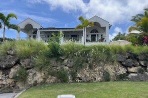 A two-story house with a stone retaining wall and lush greenery.