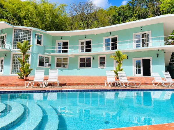 A poolside view of a two-story building with a light blue exterior, white railings, and a tiled pool with a blue border. - Torraille Waterfall Villas (Soufrière)