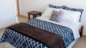 Un lit avec une couvre-lit à motifs géométriques, un plaid marron et deux coussins à motifs géométriques.