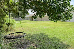 A backyard with a hanging swing chair, a lawn, and a house in the background. - The Atlantic Anchor Retreat |  30 Mins to Beach (Palm Bay)
