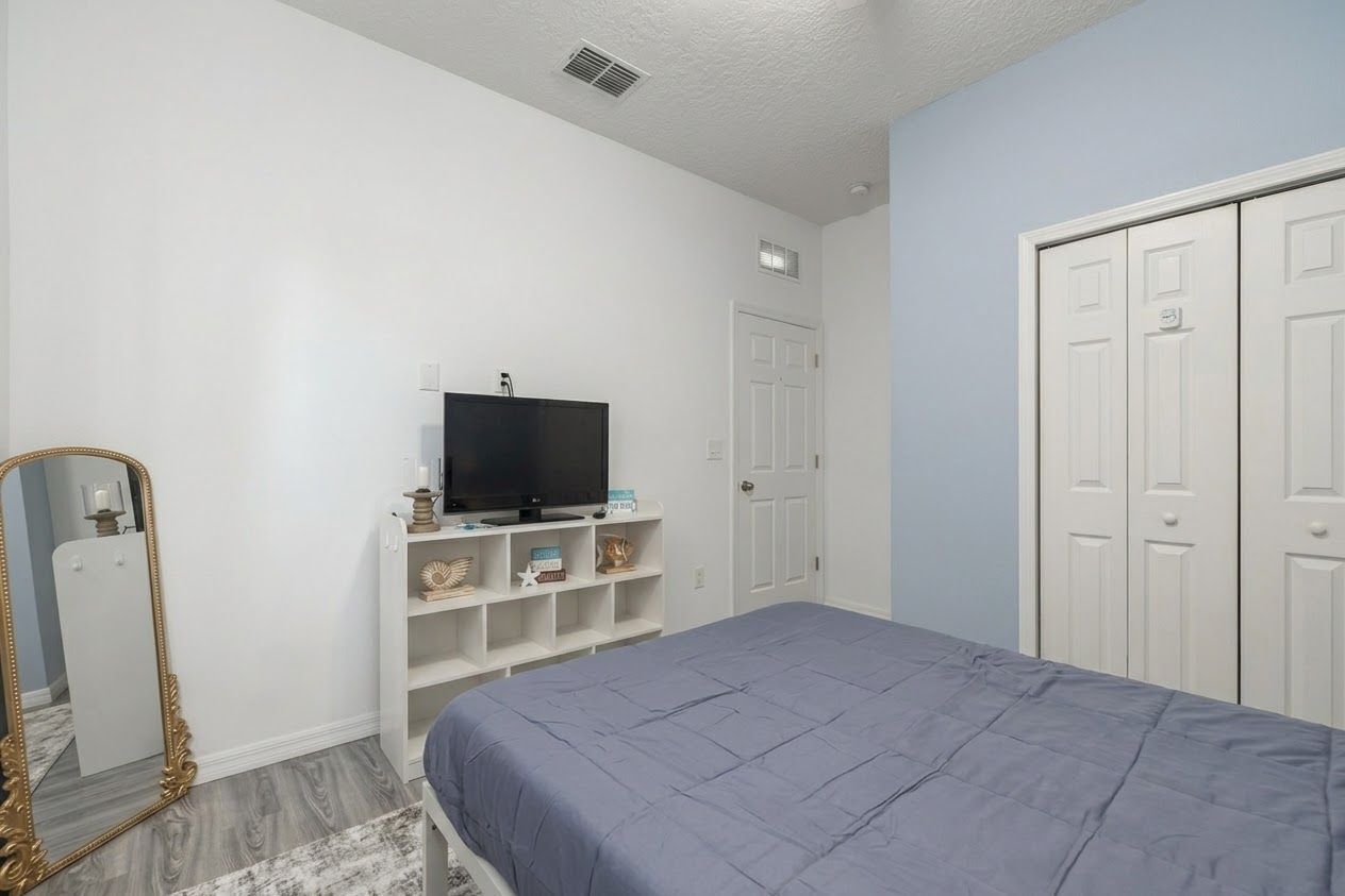 Un dormitorio con cama, televisor en una estantería, armario y espejo.