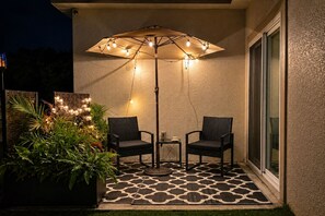 Eine Terrasse im Freien mit zwei Stühlen, einem Tisch und einem dekorativen Sonnenschirm mit Lichterkette.