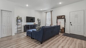 Una sala de estar moderna con un sofá azul oscuro, un televisor de pantalla plana y suelo de madera.
