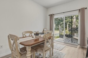 A dining area with a wooden table and chairs, a small side table with a candle holder, and a view through a glass door to an outdoor patio.