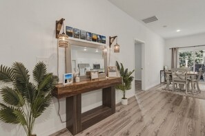 A modern interior with a wooden console table, a large mirror, and a dining area with a table and chairs.