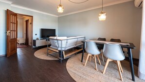 A modern living room with a sofa, dining table, chairs, and a TV. - The Porto Wine Cellars Penthouse (Vila Nova de Gaia)