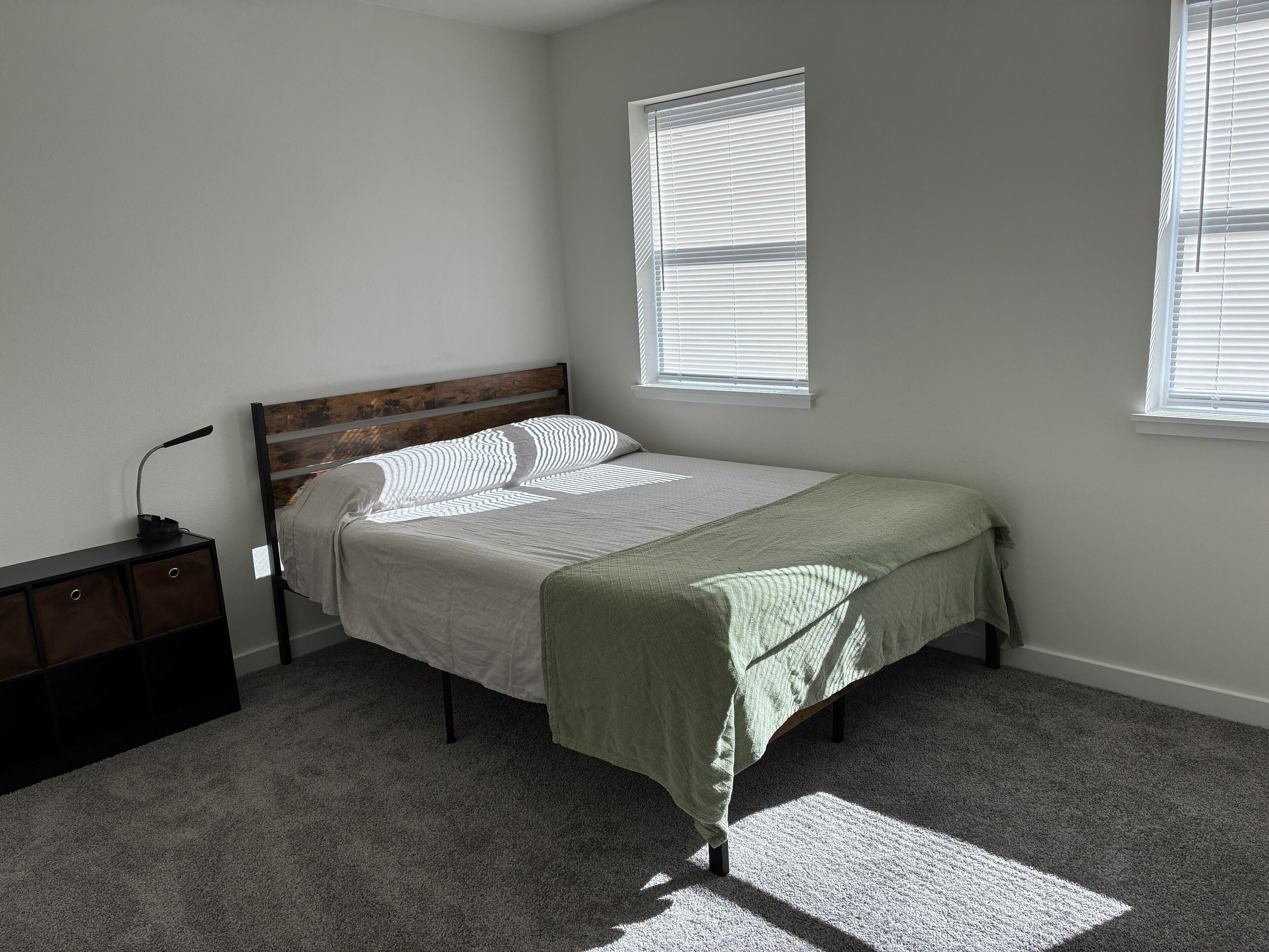 A bedroom with a bed, a nightstand, and two windows.