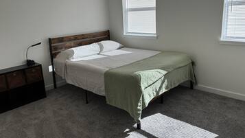 A bedroom with a bed, a nightstand, and two windows.