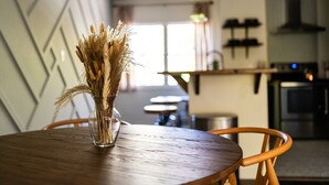 A dining table with a vase of dried wheat stalks, a wooden chair, and a kitchen in the background.