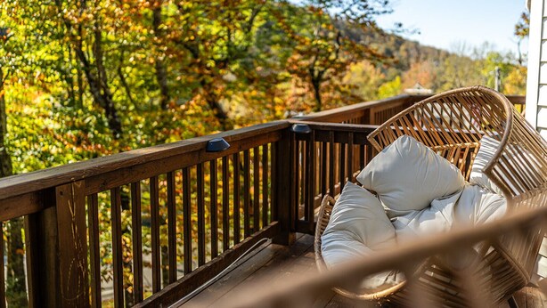 A wicker chair with a cushion on a wooden deck overlooking a forested area.