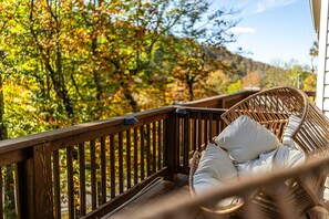 A wicker chair with a cushion on a wooden deck overlooking a forested area. - Modern Beech Mountain retreat. 3 bedrooms. Fireplace. View of the Slope (Beech Mountain)