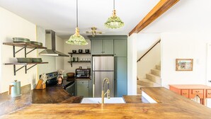 A kitchen with a wooden island, stainless steel appliances, and hanging green pendant lights.