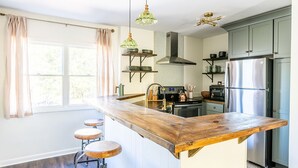 A kitchen with a wooden island, bar stools, a stainless steel refrigerator, and pendant lighting.