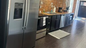 A modern kitchen with a stainless steel refrigerator, black cabinets, and a brick wall backsplash.