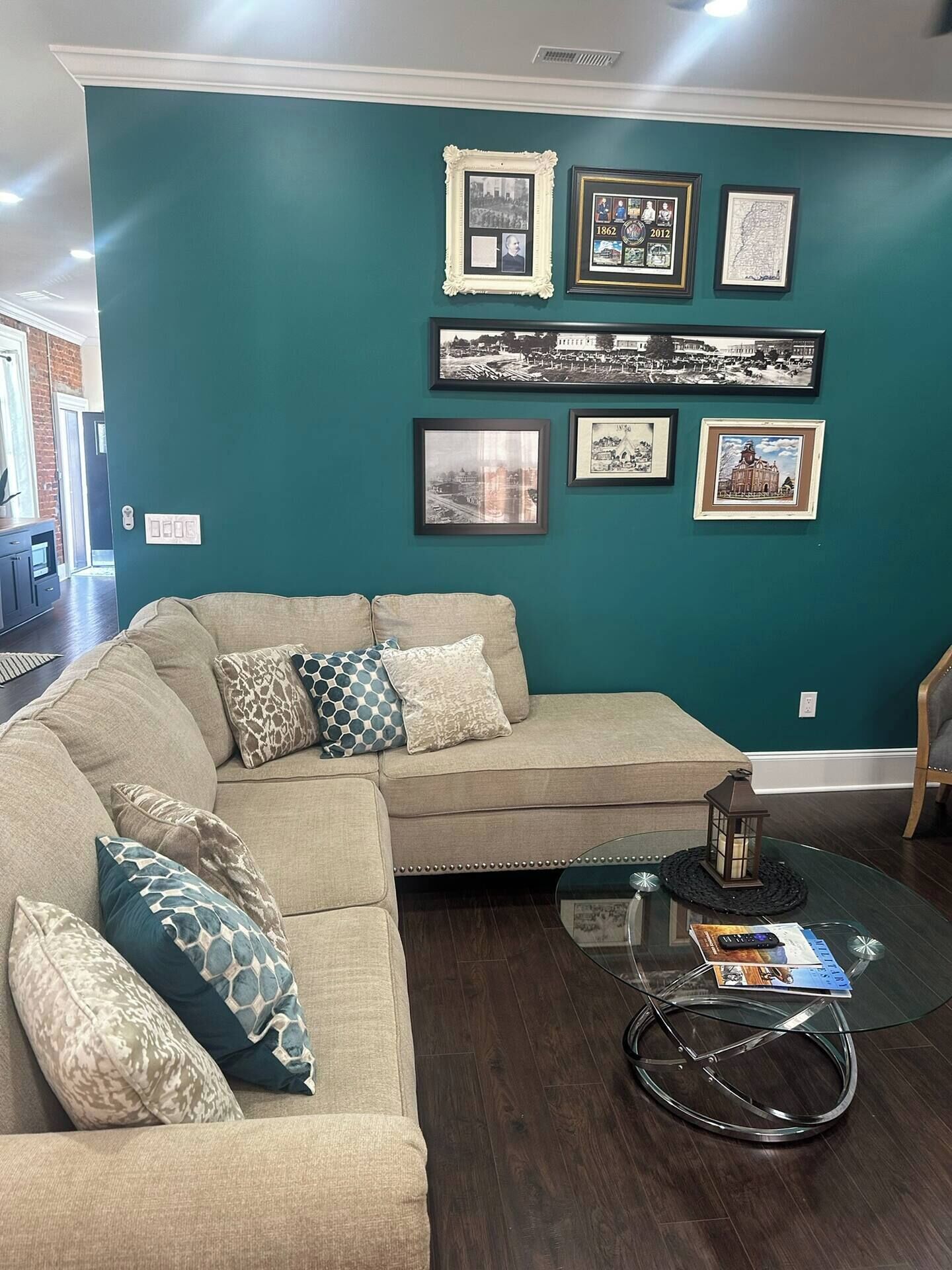 Ein Wohnzimmer mit einer türkisfarbenen Wand, einem Ecksofa und einem Couchtisch mit Glasplatte.